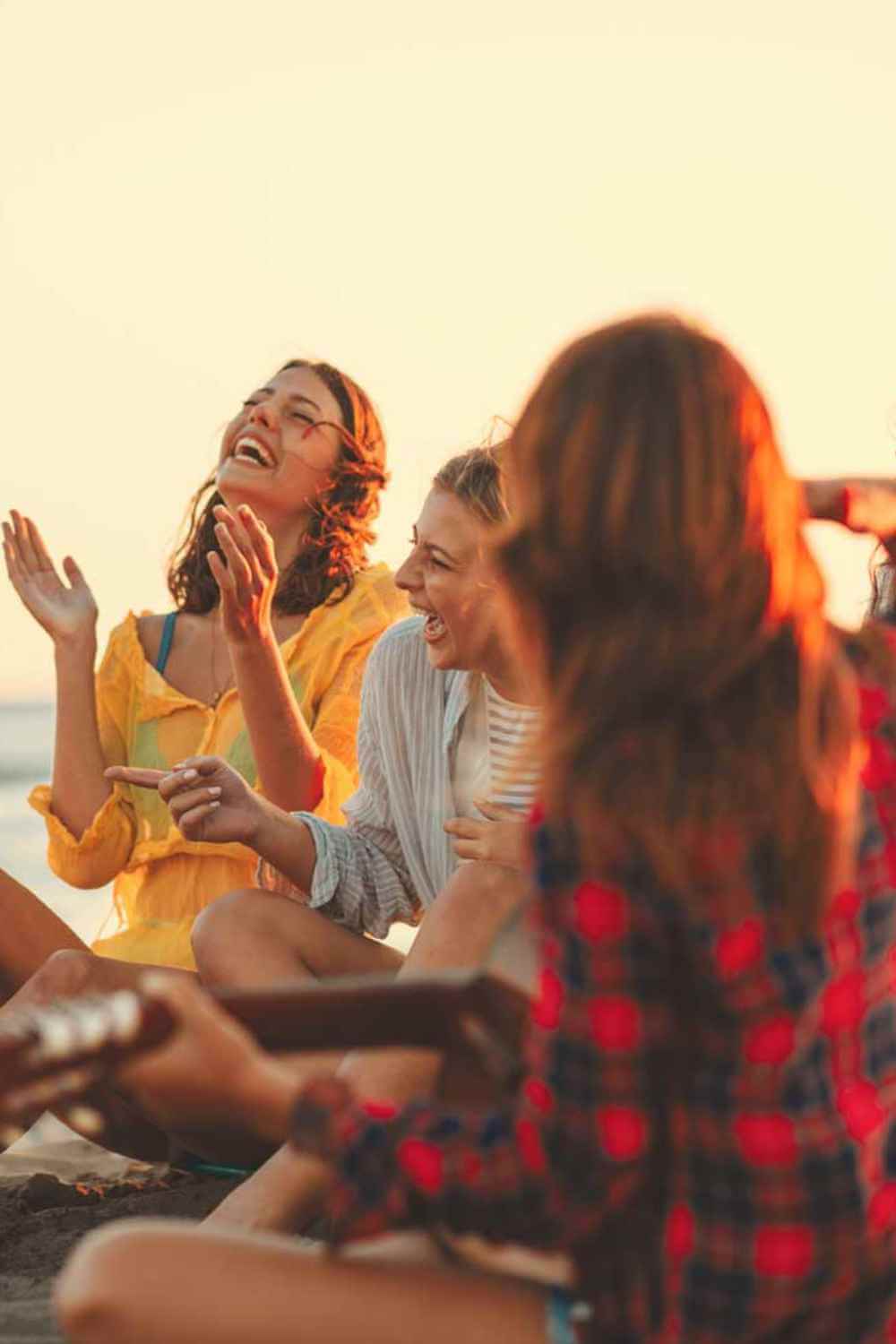 A group of friends playing guitar on the beach.