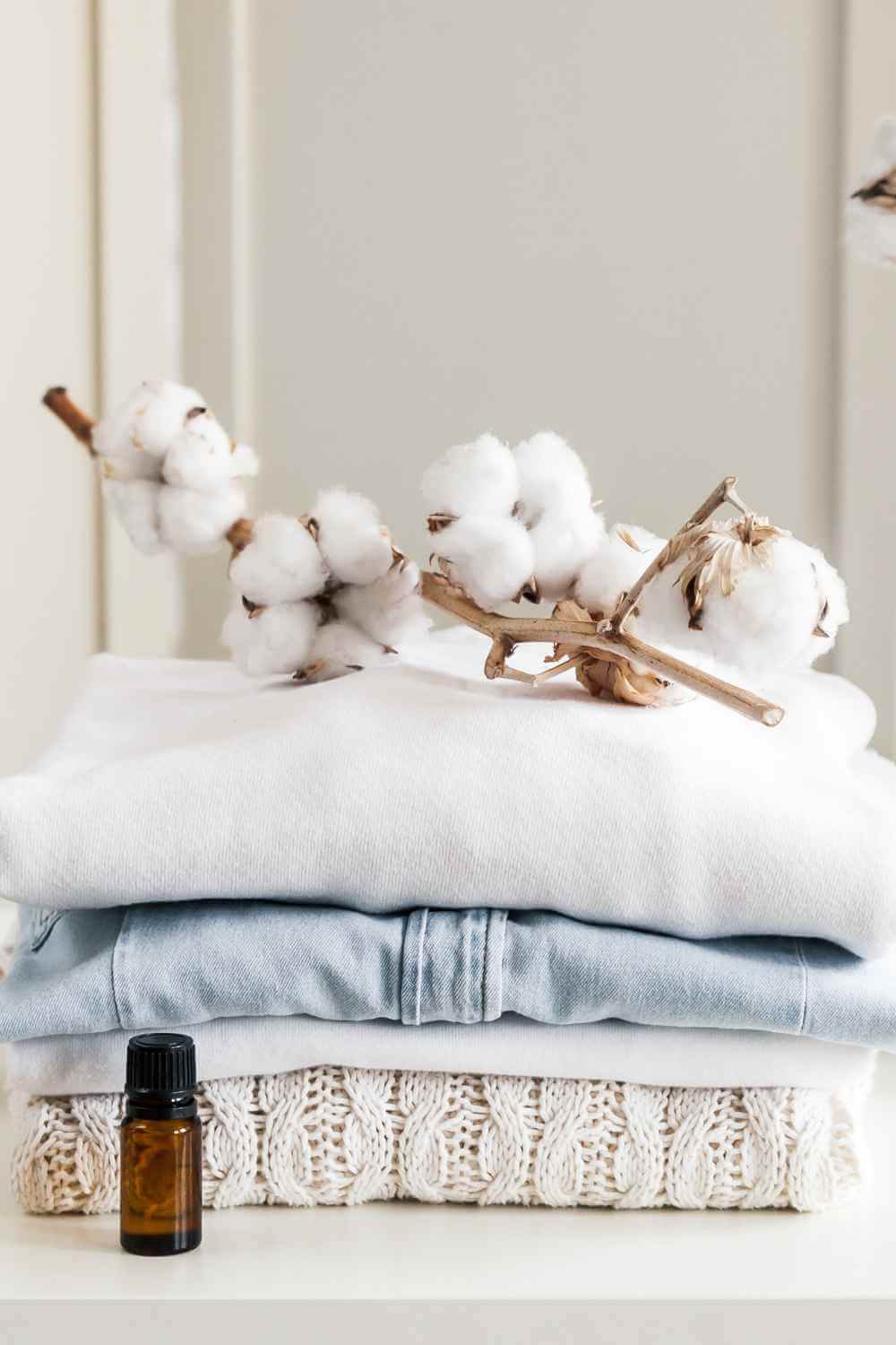 A stack of white cotton clothes and an essential oil bottle on a white table.